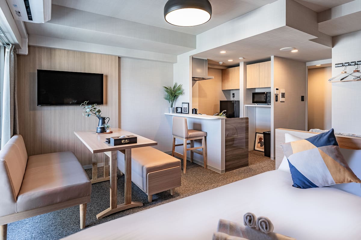 A modern hotel room with a sofa, a small table, a desk, a bed, and a kitchenette.