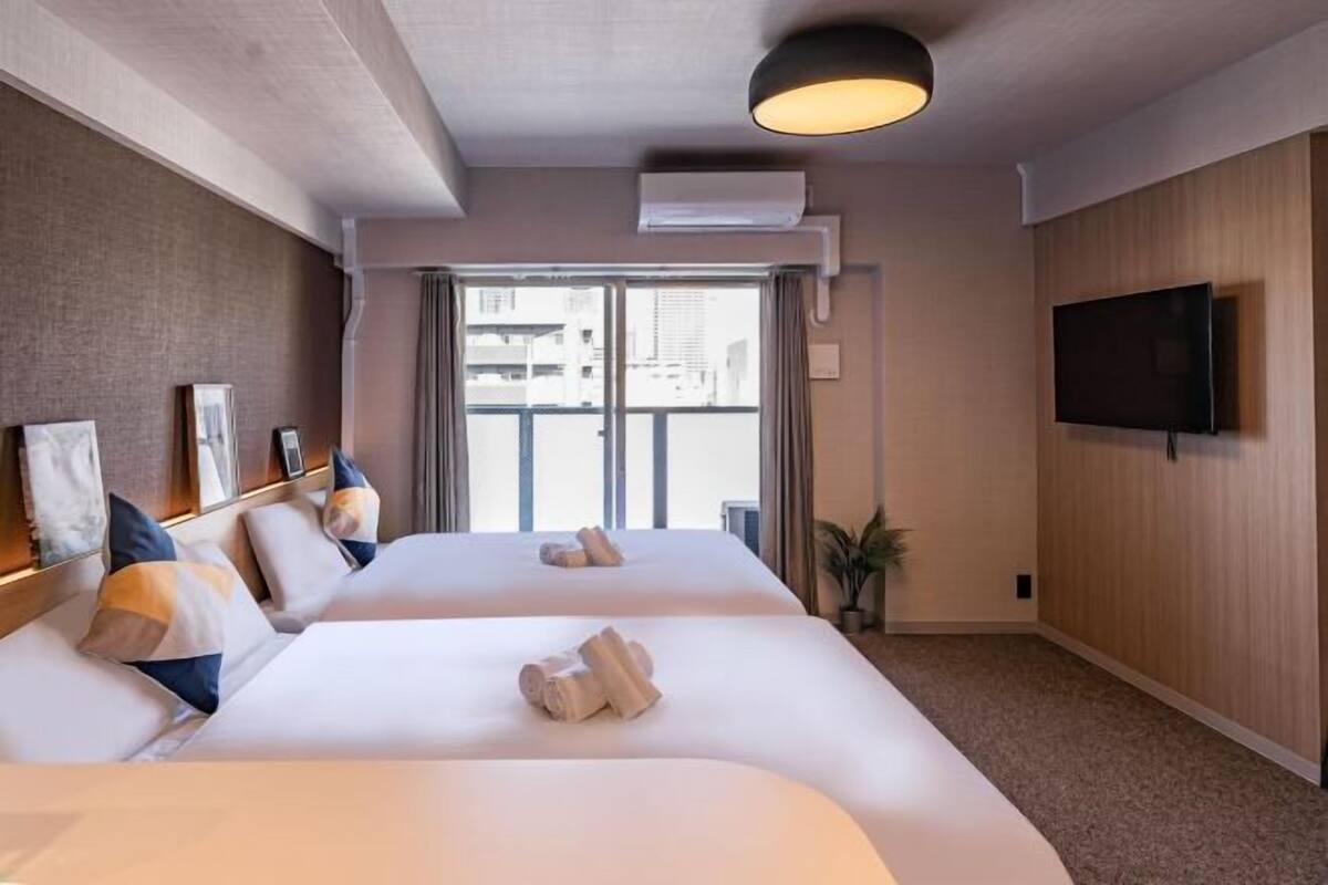 Habitación de hotel con dos camas, televisión, un ventanal grande y ventilador de techo.