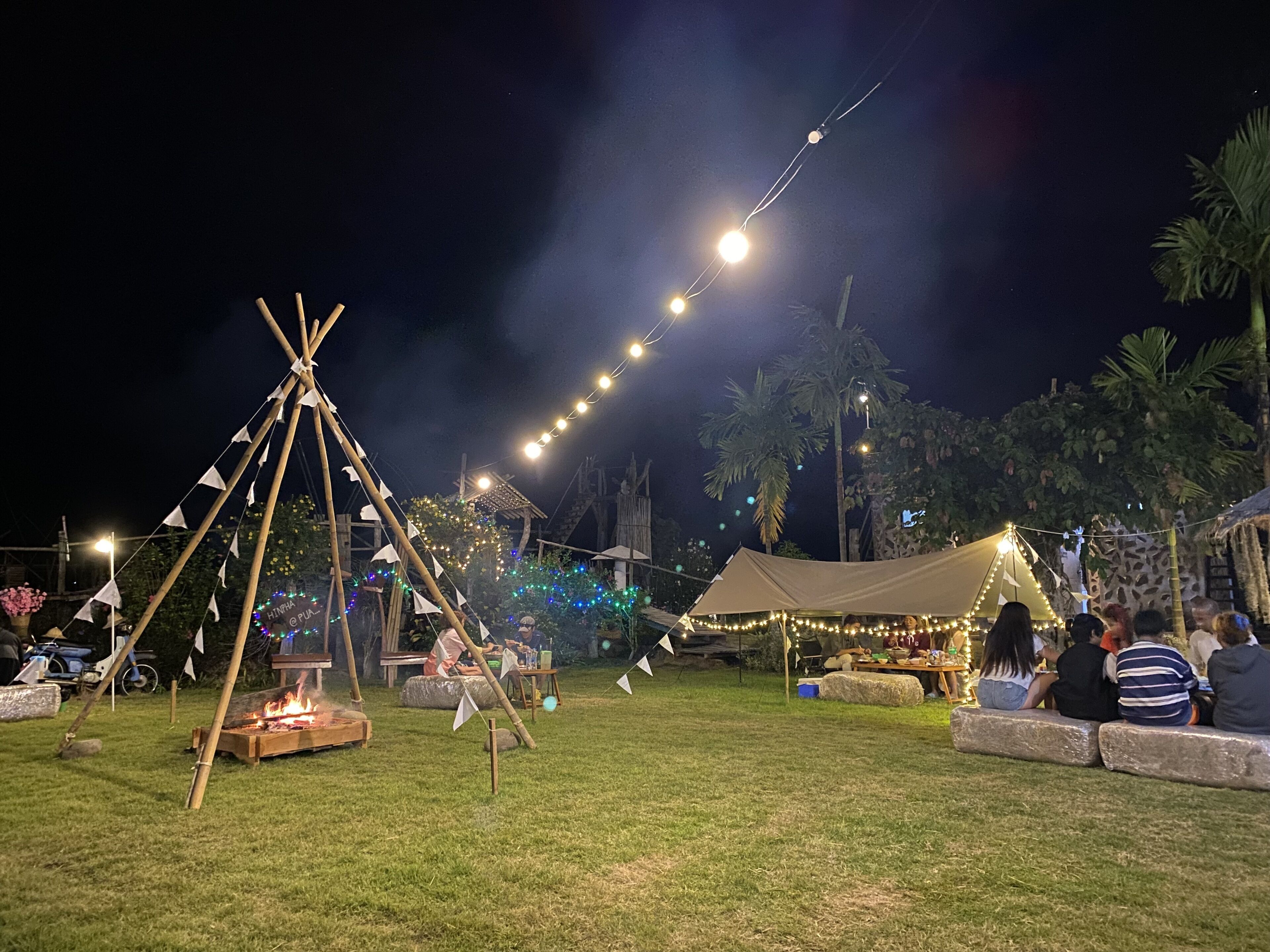 A campsite with tents, a fire pit, and string lights.