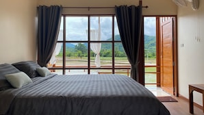 A bedroom with a large bed, curtains, a fan, and a view of a green landscape through a window. - Hinpha homestay (Pua)