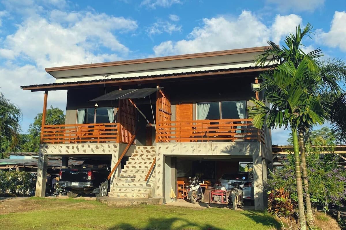 Un bâtiment à deux étages doté d’un balcon, d’un escalier et d’un garage où se trouvent des véhicules.