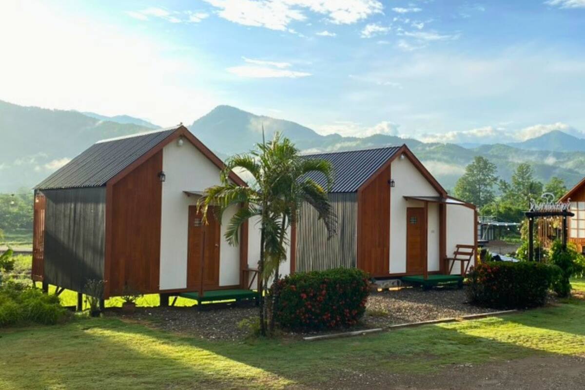 Deux cabanes en bois offrant une vue sur les montagnes, entourées de verdure et sous un ciel dégagé.