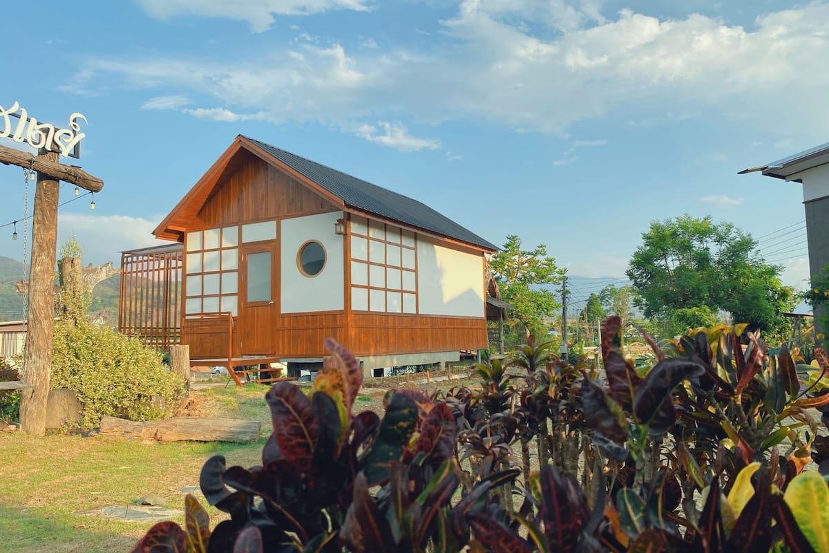 Un bâtiment traditionnel en bois, doté de grandes fenêtres et d’un toit en pente, entouré de verdure.