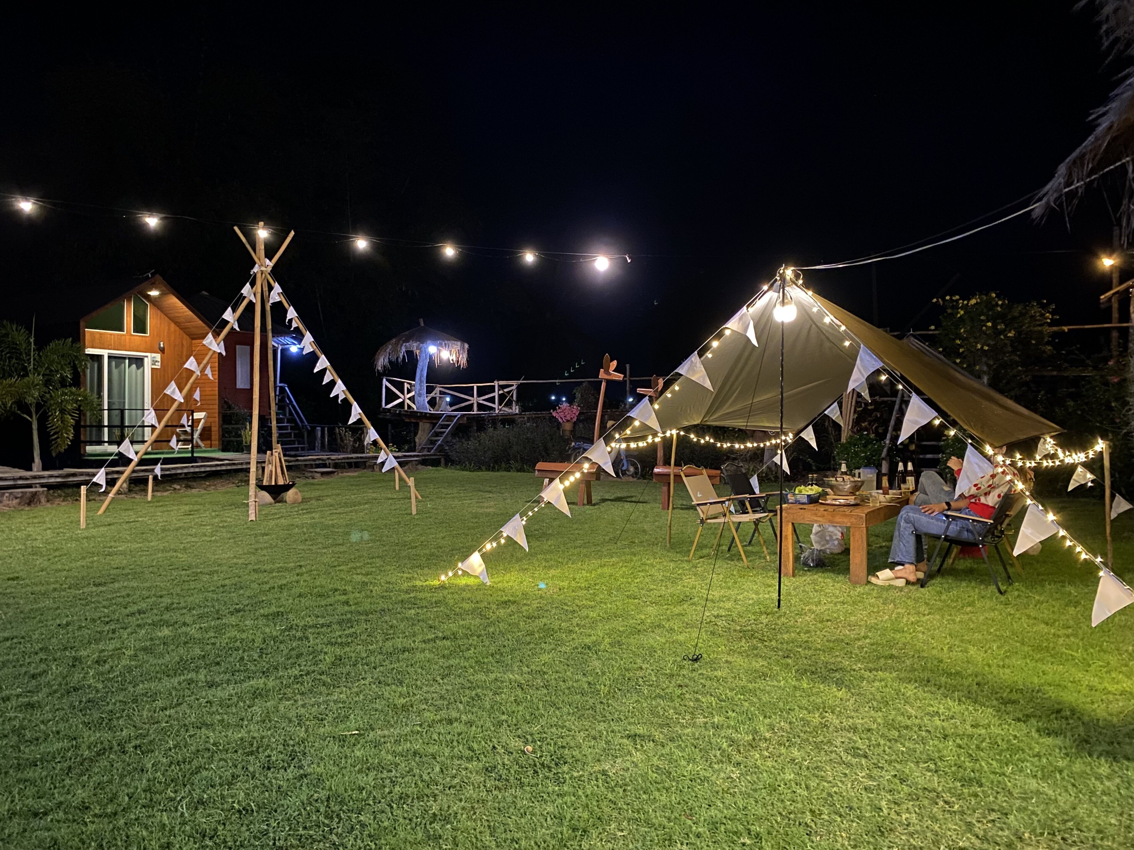 Un espacio al aire libre con carpas, luces colgantes, una estructura de madera y una pequeña mesa con sillas.