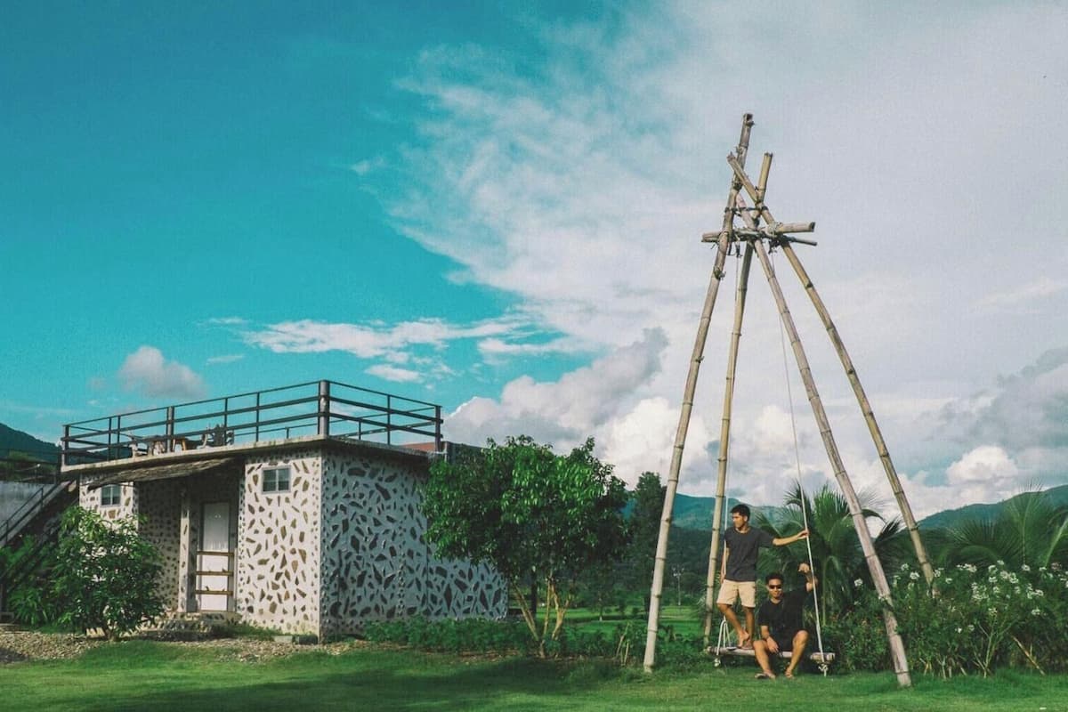 Une maison avec un balcon, une balançoire et une personne assise sur la balançoire.