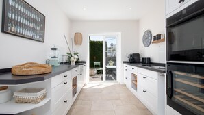 A modern kitchen with white cabinets, a large oven, and a dining area visible through glass doors. - Relax - Denia, Costa Blanca (Denia)