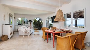 A spacious living area with a dining table, wicker chairs, and a large window offering a view of the outdoors. - Relax - Denia, Costa Blanca (Denia)