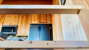A wooden staircase leading to a kitchen area with wooden cabinets and a refrigerator. - Alpine Meadows Cabin

 (Homer)