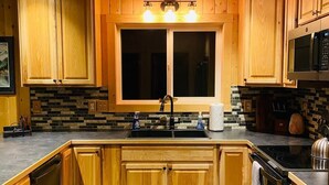 A modern kitchen with wooden cabinets, a large window, and a black countertop. - Alpine Meadows Cabin

 (Homer)