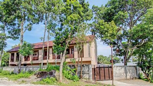 A two-story building with a red-tiled roof, surrounded by greenery and a gated entrance. - OYO Life 93497 Griya Kost Rr (Salatiga)