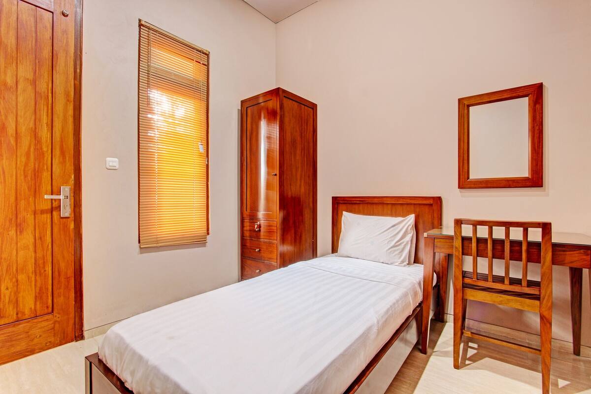 A bedroom with a single bed, wooden wardrobe, and a desk with a chair.