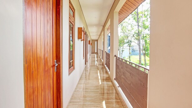 A corridor with wooden doors and windows, leading to a balcony with a view of trees and a building. - OYO Life 93497 Griya Kost Rr (Salatiga)