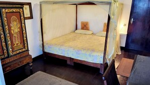 A room with a four-poster bed, a wooden cabinet with a religious icon, a chair, and a door. - Beach Villa Yin Near Hikkaduwa, With Pool and Cook - Semi-detached House (Hikkaduwa)