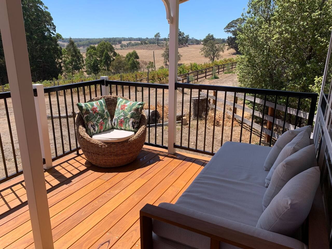 A wooden deck with a wicker chair and a sofa facing a vineyard.