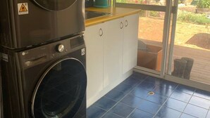 A laundry area with stacked washers and dryers, a sink, and a window overlooking a garden. - Belmira Vines
 Private Vineyard Escape! (Kangaroo Gully)