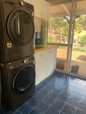 A laundry area with stacked washers and dryers, a sink, and a window overlooking a garden. - Belmira Vines
 Private Vineyard Escape! (Kangaroo Gully)