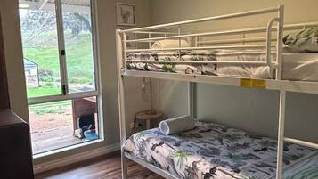 Een slaapkamer met stapelbed, een plafondventilator, een raam met uitzicht op de omgeving en een houten vloer.