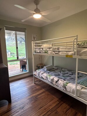Une chambre avec un lit superposé, un ventilateur de plafond, une fenêtre donnant sur l’extérieur et un plancher en bois.