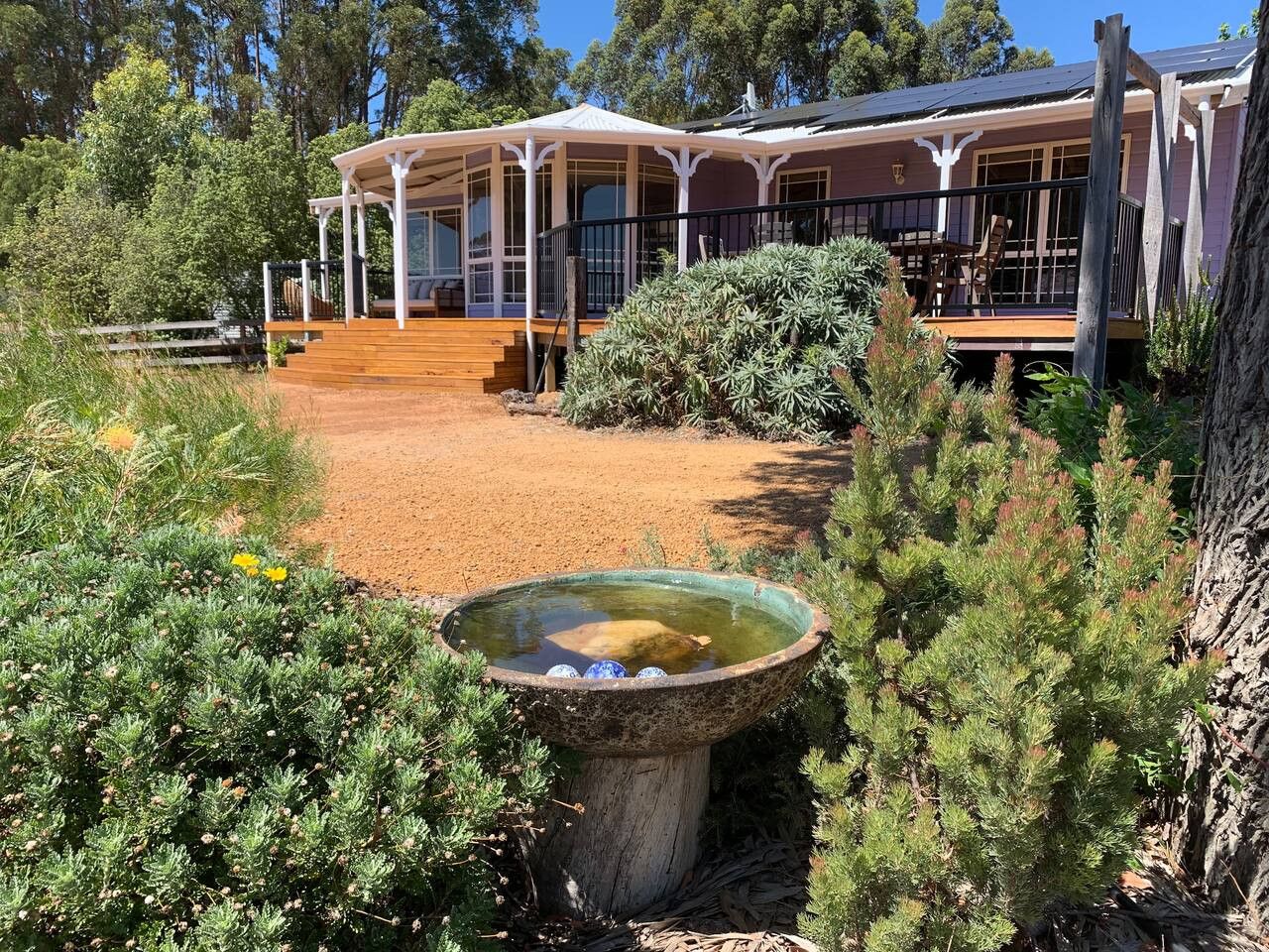 A rustic house with a covered porch, a wooden deck, and a bird bath.