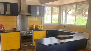 A modern kitchen with a central island, yellow and blue cabinetry, and a large window providing a view of the outdoors. - Belmira Vines
 Private Vineyard Escape! (Kangaroo Gully)