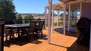 Une terrasse en bois avec un espace patio couvert, une table et des chaises, ainsi qu’un barbecue.