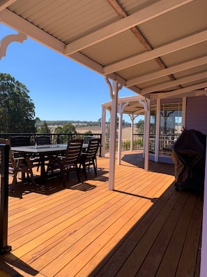 Una terraza de madera con un porche cubierto, una mesa, sillas y una parrilla.