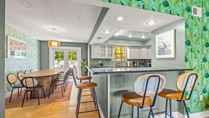 A modern kitchen with a central island, bar stools, and a dining area with a long table and chairs.