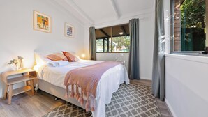 Une chambre à coucher avec un lit, une table de chevet, une lampe et une fenêtre avec des rideaux.