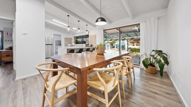 Un espace repas moderne avec une table en bois et des chaises en osier, une cuisine en arrière-plan et une grande fenêtre avec des rideaux.