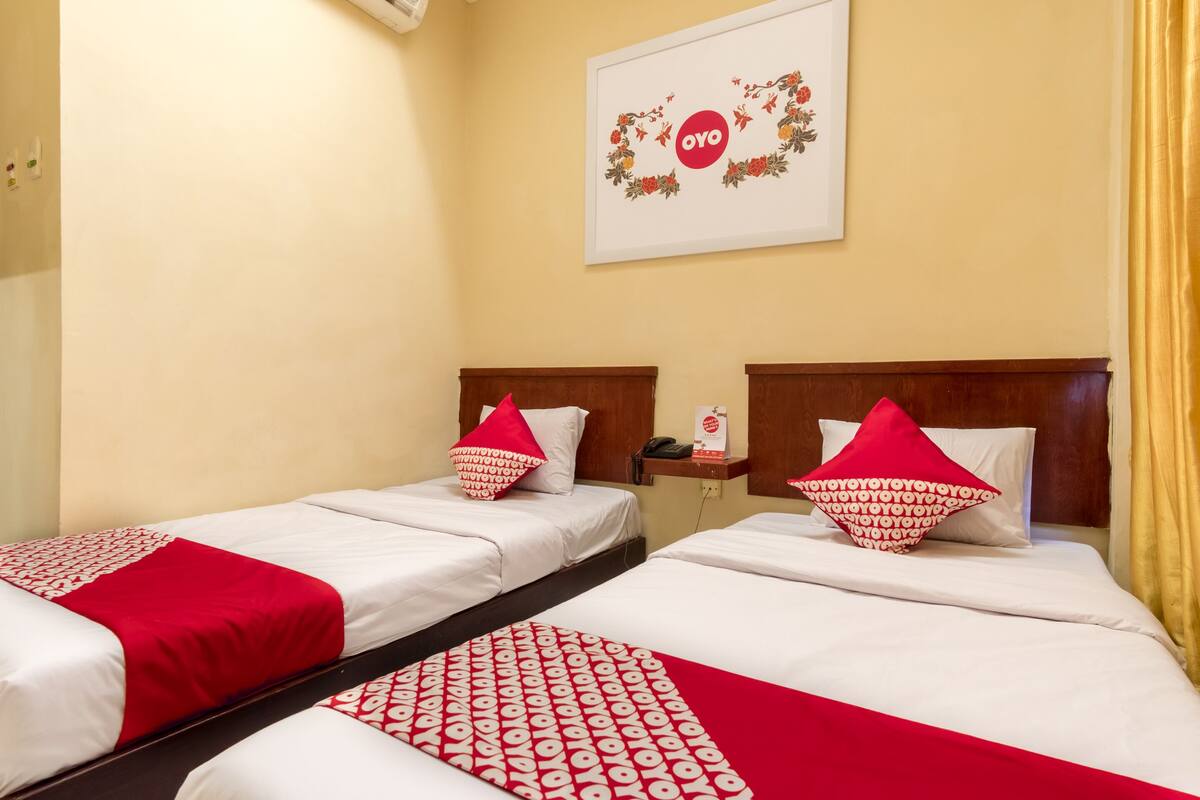 Ein Hotelzimmer mit zwei Betten, jeweils mit einer rot-weißen Musterdecke und passenden Kissen. Über den Betten befindet sich ein gerahmtes Kunstwerk mit dem Schriftzug "OYO".