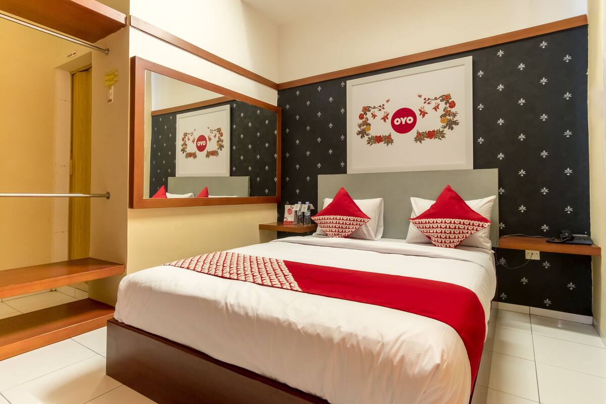 Ein modernes Hotelzimmer mit einem großen Bett, einem Nachttisch, einem Spiegel und einem Kleiderschrank.
