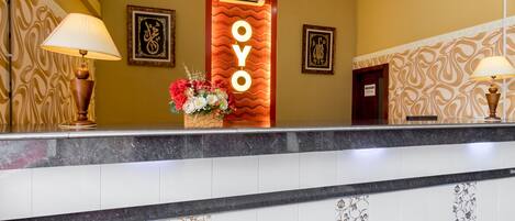 Una reception di hotel con un bancone in marmo, un'ampia insegna illuminata 'OYO', decorazioni a parete a motivi decorativi e due lampade.