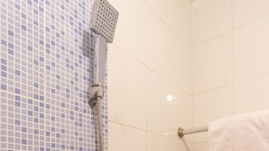 Un espace douche avec des carreaux de mosaïque bleus, une serviette blanche et un pommeau de douche.