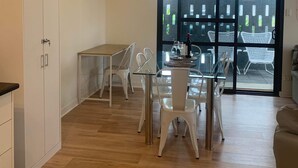 A modern kitchen with white cabinets, a dining area with a glass table and white chairs, and a large sliding glass door leading to an outdoor patio with white chairs and a black fence.