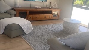 A modern living room with a wooden entertainment unit, a large flat-screen TV, a grey rug, and a round white side table.