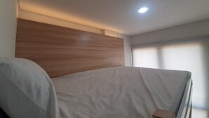 Un dormitorio con cabecera de madera, cubrecama blanco y una pequeña caja de cartón en el suelo.