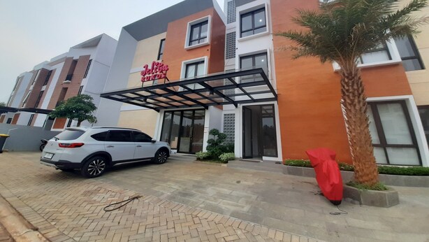 Entrada de hotel moderna con un camino techado, un coche blanco estacionado y una palmera.