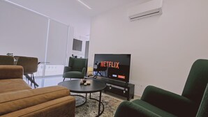 Moderni olohuone, jossa on suuri litteänäyttöinen televisio, jonka näytöllä näkyy Netflixin logo. Huoneessa on myös sohva, nojatuoli ja sohvapöytä.
