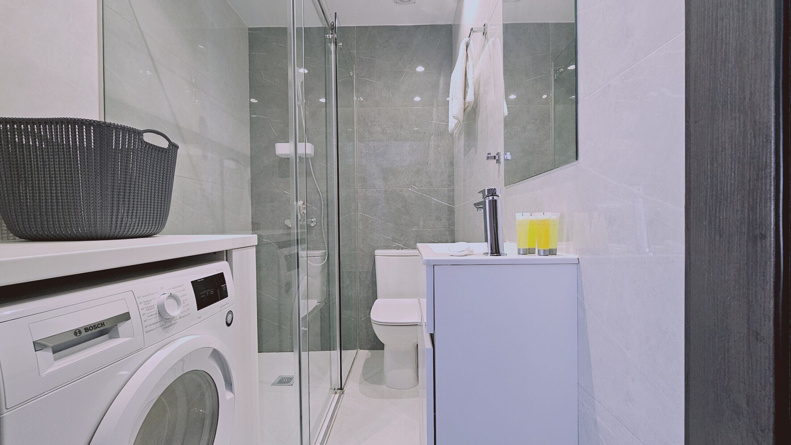Ein modernes Badezimmer mit einer Duschkabine aus Glas, einer Waschmaschine von Bosch und einem Waschbecken mit Toilettenartikeln.
