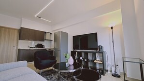 A compact living space with a kitchenette, a flat-screen TV, a sofa, a coffee table, and a floor lamp. - STAY Cosmo City Suite 302 (Nicosia)