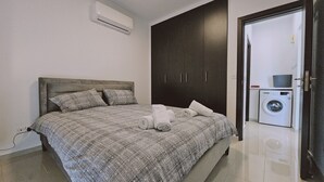 Une chambre à coucher avec un lit, une armoire sombre et un lave-linge dans la pièce adjacente.