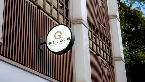Een hotelschild met de naam 'HOTEL G-CUE' en de locatie 'OSAKA TANIMACHI'.