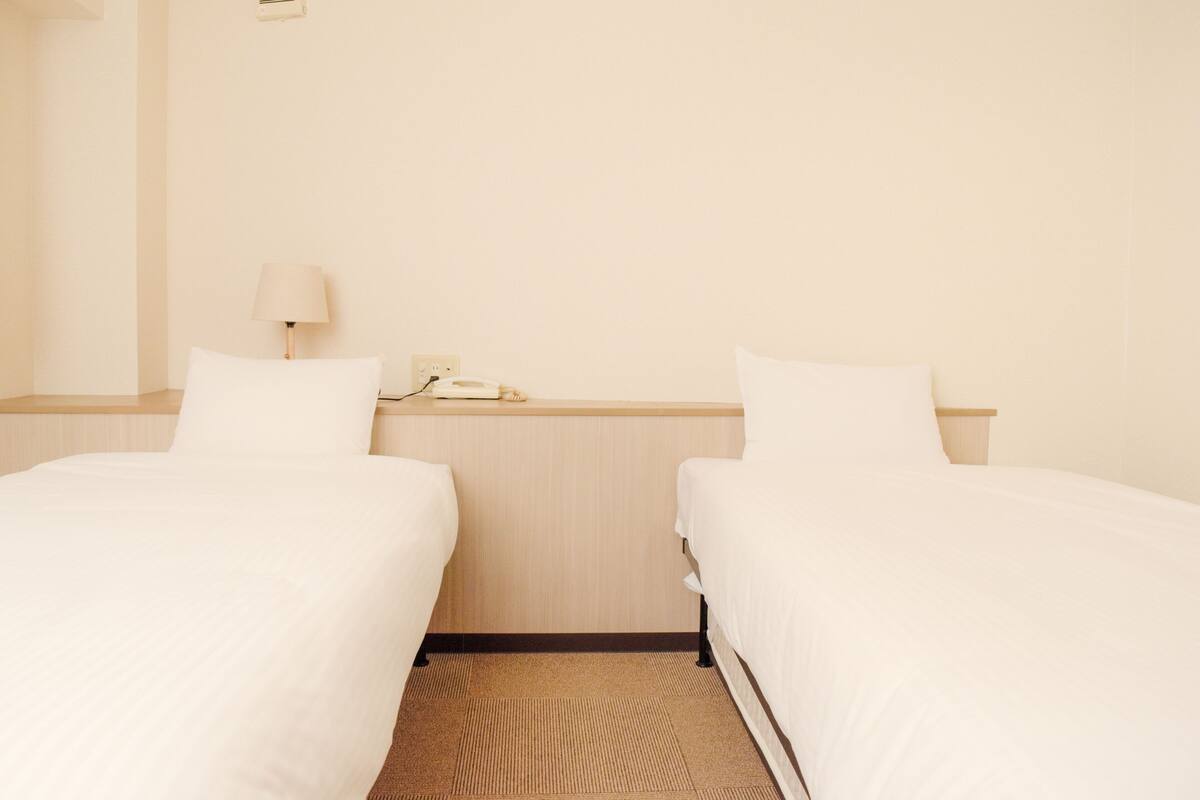 Una habitación de hotel con dos camas individuales, una mesita de noche con lámpara y un teléfono.