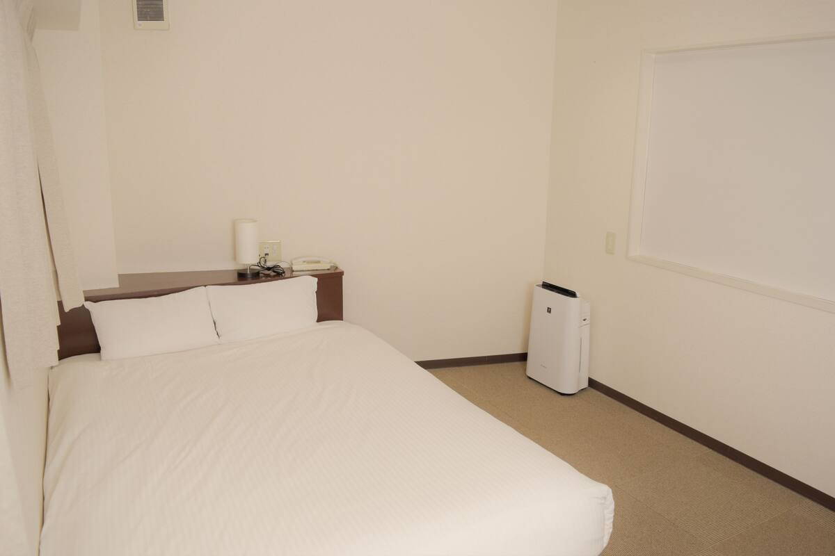 Una habitación de hotel con cama, mesita de noche, lámpara, teléfono y cesto de basura.