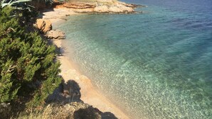 Paesaggio costiero con acque cristalline, una spiaggia sabbiosa e vegetazione.