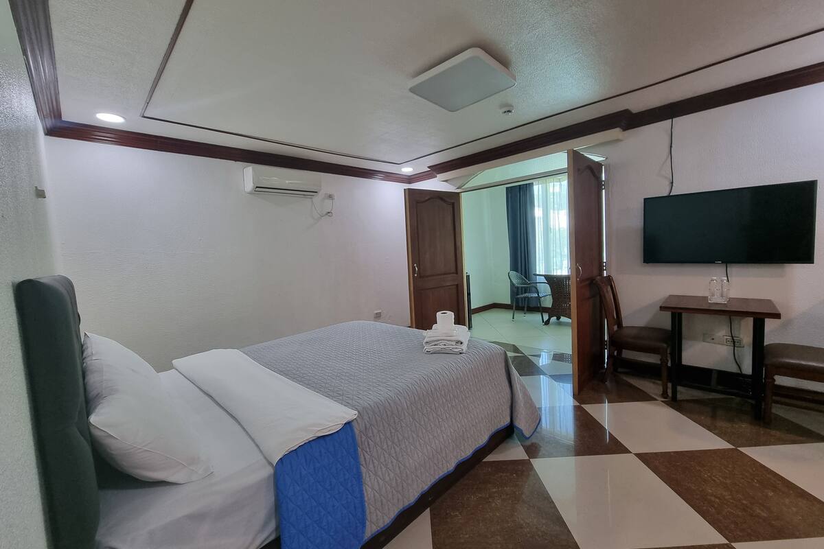 A hotel room with a bed, a TV, a small table with a bottle, and a chair.