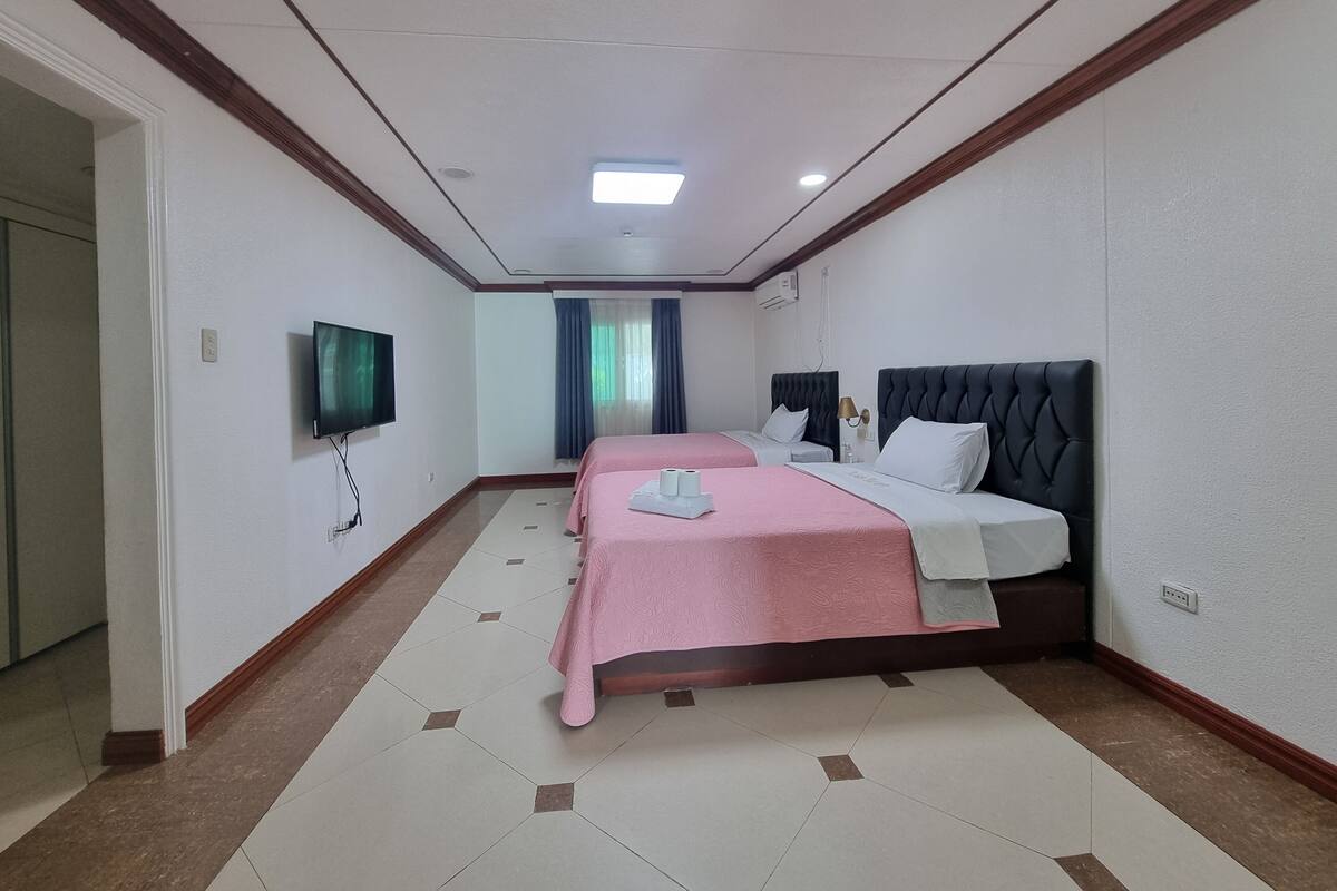 A hotel room with two beds, a television, and a bathroom visible in the background.