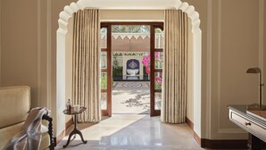 A hallway with a view of a courtyard, a small table with a cup, and a lamp on a side table.