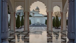 A courtyard with a fountain, surrounded by columns and a patterned floor, leading to a white building with domes.