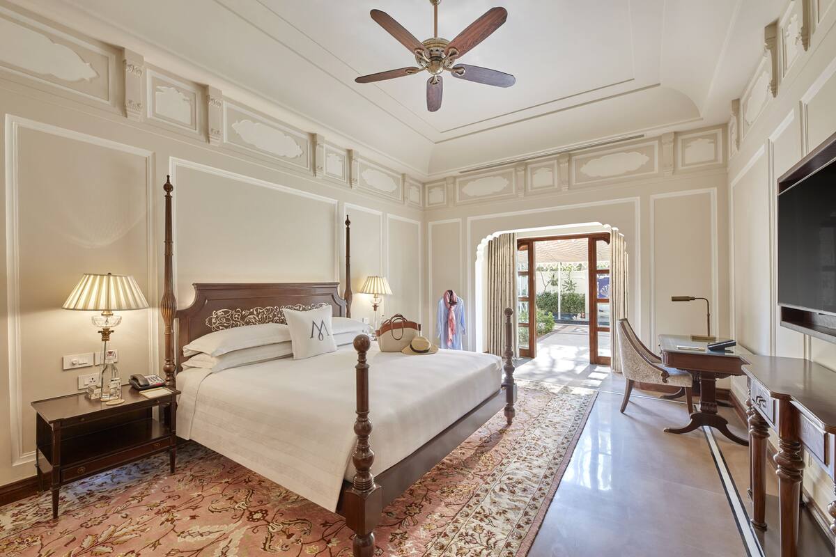 Habitación de hotel con cama con dosel, ventilador de techo, televisor y vistas al exterior.